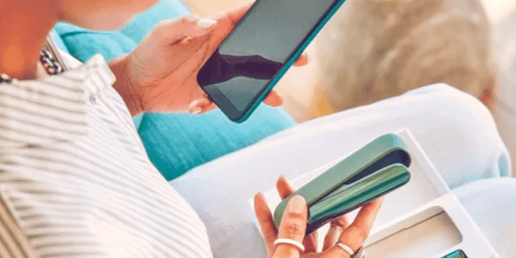 One woman holding holding a phone and an IQOS device.