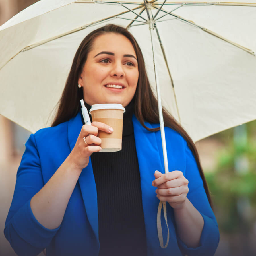 Femeie cu o umbrelă, ținând în mână un pahar de hârtie cu cafea și un dispozitiv IQOS